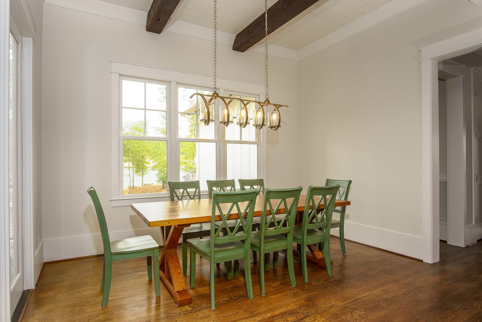 Picture of well-lit dining area featuring green chairs and a long, wood-finished table.